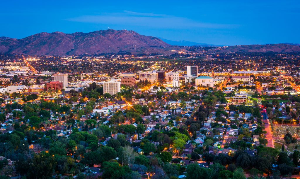 Evening cityscape with illuminated buildings and mountains in the background.
